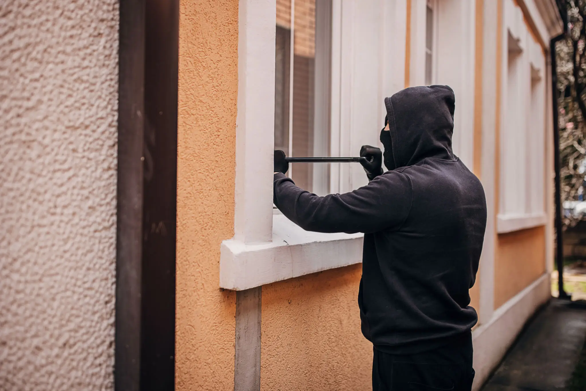Hooded person using crowbar at window